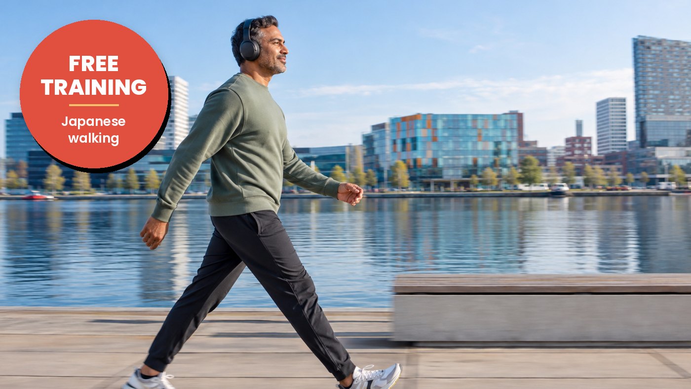 Man wearing headphones walks briskly along the water, with the city behind him